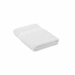 A white bath towel neatly folded, featuring a textured surface and a simple design. It has a subtle branding logo.