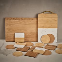 A wooden serving board with a built-in handle, featuring a marble section and various wooden and cork coasters.