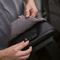 A backpack with a grey flap and a TSA lock, featuring anticut fabric and a sleek black design.