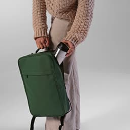 A green backpack with a laptop compartment and a front pocket, held by a person alongside a drink bottle.
