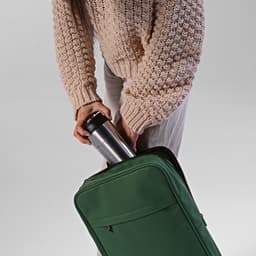 A green backpack with a silver drink bottle being placed inside. The person is wearing a knitted sweater.