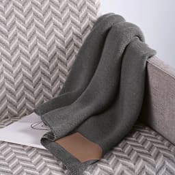 A grey wool blend blanket with a customisable patch draped over a textured sofa.