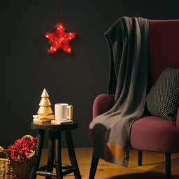A grey wool blend blanket drapes over a maroon chair beside a small table with a white mug and decorative items.