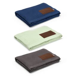 Three folded Giotto Blankets in navy blue, light green, and dark grey, each featuring a customisable brown patch.