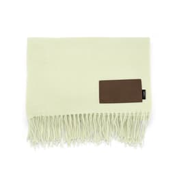 A light green blanket with fringes and a brown customisable patch. It features a logo on the patch.