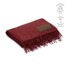 A maroon blanket with fringed edges and a brown customisable patch. Features sustainable materials.