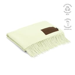 A pale green blanket made from sustainable materials, featuring a brown customisable patch and fringe detailing.