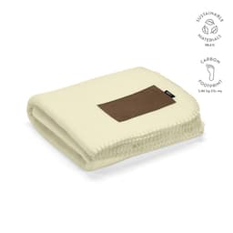 A folded cream blanket with a brown patch, featuring stitching details and a logo. Made from sustainable materials.