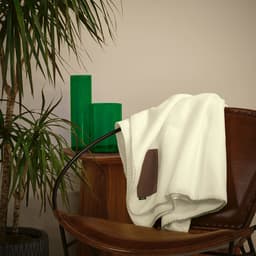 A white blanket draped over a chair with a brown patch, beside green decorative items and a plant.