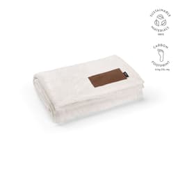 A cream blanket made from sustainable materials, featuring a customisable brown patch. It is neatly folded.