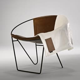 A cream blanket drapes over a modern metal and leather chair, featuring a customised patch on the blanket.