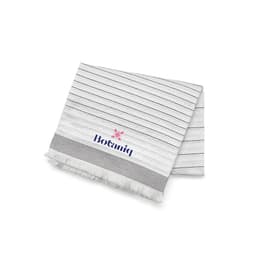 A striped, white cotton blanket with navy lines and fringed edges, featuring a logo.