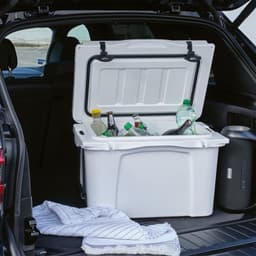 A white cooler with a lid is open in a vehicle, containing various bottles and a towel inside.