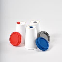A set of ceramic travel cups in white with grey, blue, and red lids, featuring a logo on one cup.