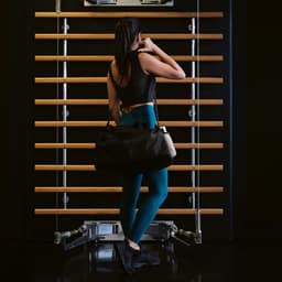 A black gym bag is being held by a person in fitted workout clothes, with reflective strips visible.