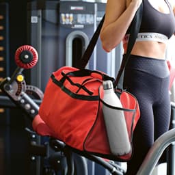 A red gym bag with black accents, featuring a reflective strip, alongside a drink bottle, on a gym equipment.