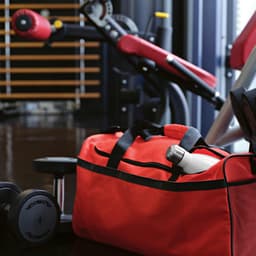 A red gym bag with reflective strips, featuring a drink bottle peeking out, rests on a gym floor.