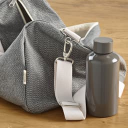 A grey gym bag with a white strap beside a grey drink bottle, set on a wooden surface.