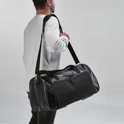 A black gym bag with waterproof zippers, held by a person wearing a grey sweatshirt. The bag has a logo visible.