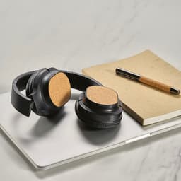 A pair of black headphones with cork ear cushions rests on a laptop, alongside a notebook and a pen.