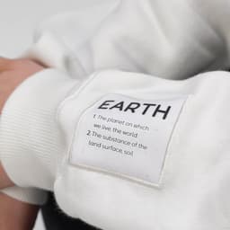 A white sweatshirt with a tag featuring the word "EARTH," made from organic cotton and rPET, with a branded logo.
