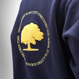 A navy sweatshirt featuring an embroidery design of a tree and a circular logo. Made from organic cotton and recycled materials.