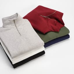 A stack of four Malibu 1/4 zip sweatshirts in grey, maroon, green, and navy, featuring a logo on one.