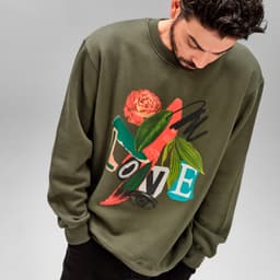 A green crew neck sweatshirt featuring a floral and abstract graphic design, worn by a model.