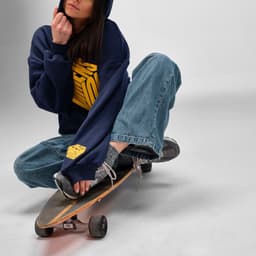 A navy oversized hooded sweatshirt with a logo, worn by a person sitting on a skateboard, paired with blue jeans.