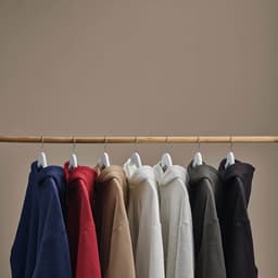 A collection of oversized hooded sweatshirts in navy, burgundy, beige, white, grey, and black, hanging on a wooden rack.