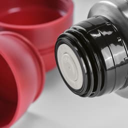 A drink bottle in metallic silver with black screw cap, accompanied by two red cups. It includes a carabiner.