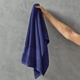 A hand holds a deep blue cotton towel with textured stripes, showcasing its soft material.