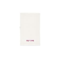 A cream-coloured towel made of cotton with a branding logo, featuring the words "SELF CARE" in burgundy.