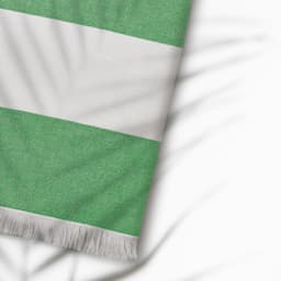 A green and white striped towel with fringing, made from cotton and featuring a logo.