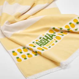 A yellow towel featuring a striped design with pineapples, including a logo. Soft and made from cotton.