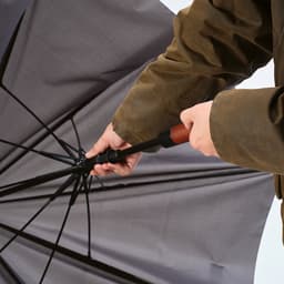A grey windproof umbrella with an automatic opening feature, being held by a person in a brown jacket.