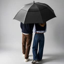 A black golf umbrella with a storm-proof design, featuring automatic opening, held by two people walking together.