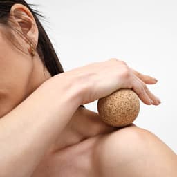 A cork sphere resting on a person's shoulder, with natural tones and a smooth texture. Features a simple logo.