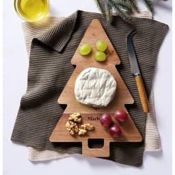 A wooden tree-shaped cheese board featuring brie cheese, grapes, walnuts, and a knife on a textured cloth.