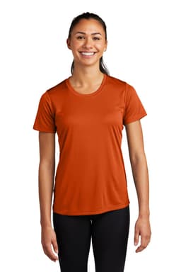 A woman wearing an orange Sport-Tek Ladies PosiCharge Competitor Tee, standing with a smile. The shirt has short sleeves.