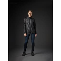A women's black thermal shell jacket with a quilted design, paired with dark jeans and boots, displayed against a dark background.