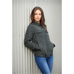 A woman leans against a wall wearing a dark green quilted jacket with buttons and chest pockets.