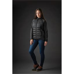 A woman wearing a black and grey Women's Narvik Hybrid Jacket with a fitted design, paired with jeans and boots.