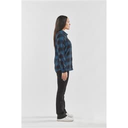 A side view of a woman wearing a blue and black checkered button-up shirt with black jeans and white shoes.