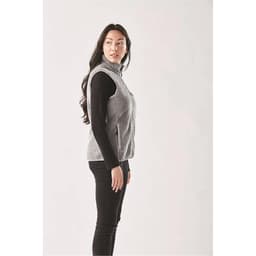 A side view of a women's grey sherpa fleece vest, worn over a black long-sleeve top, with a logo visible.