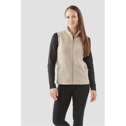 A woman models a beige full zip fleece vest, paired with a black long-sleeve top, standing against a light background.