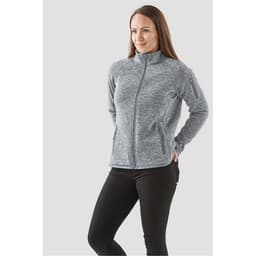 A woman wearing a grey full zip fleece jacket stands with her hands in the pockets, featuring a branding logo.