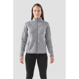 A woman is wearing a grey full zip fleece jacket with a high collar and side pockets. The jacket features a logo.