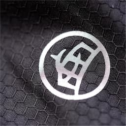 A close-up of a black textured fabric featuring a circular logo. The texture resembles a honeycomb pattern.