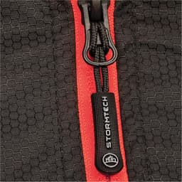 A close-up of a black thermal jacket featuring a contrasting red zipper and a branded pull tab.